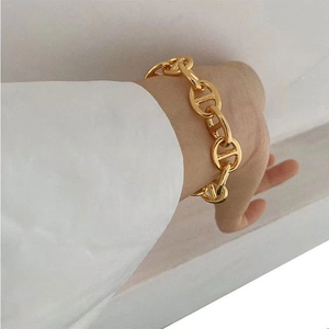 Detailed view of a gold-plated pig nose link bracelet worn on a wrist with white shirt