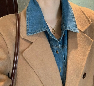 Close-up of a polished gold pig nose pendant necklace worn over a stylish denim shirt