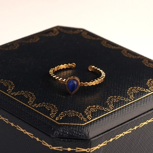 Dettaglio macro di un anello a goccia dorato vintage con gemma blu su scatola
