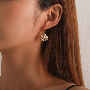 Pendientes creativos de concha dorada llevados por modelo con estilo minimalista chic