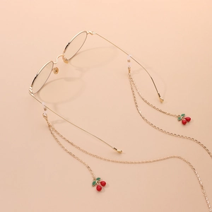 Golden eyewear chain with red cherry charms on gold frames over a soft pink background