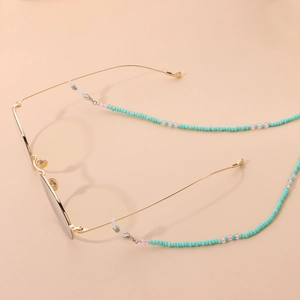 Fashionable gold frame glasses with turquoise and pink beaded strap chain on beige background