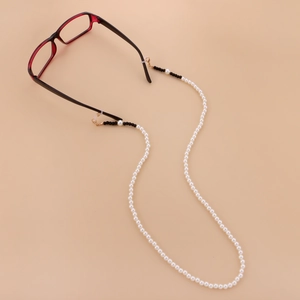 Chaîne à lunettes élégante en perles blanches avec fermoirs dorés sur fond beige neutre