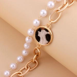 Detail der goldenen Bambuskette mit weißen Perlen und einem runden Leoparden-Anhänger