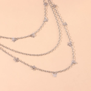 Detail shot of multi-layer silver butterfly chain accessory over a warm peach background