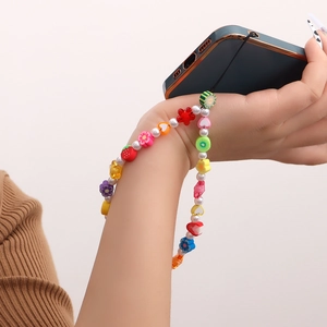 Dragonne de téléphone perlée arc-en-ciel avec breloques cœur et fruits sur le poignet d'un mannequin