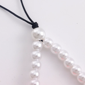 Macro view of white faux pearls and black woven cord knot details of the phone strap