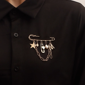 Golden safety pin brooch featuring star and letter M pendants over black fabric