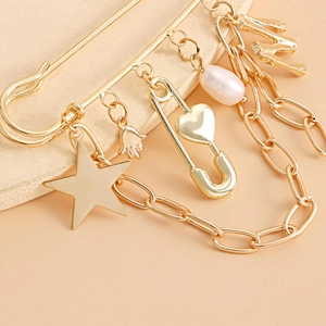 Detail shot of a gold safety pin brooch with star, pearl, and letter M fringe charms