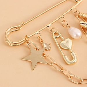 Detailed close-up of golden safety pin brooch featuring star and faux pearl pendants