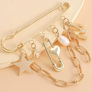 Detail of gold safety pin brooch with star, heart, and pearl charms on stone tray