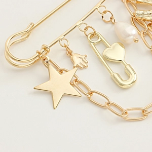 Detail of gold safety pin brooch featuring star, palm charm and thick metal chain