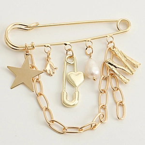Detail of gold safety pin brooch with star, M pendant, pearl, and Hamsa hand charms