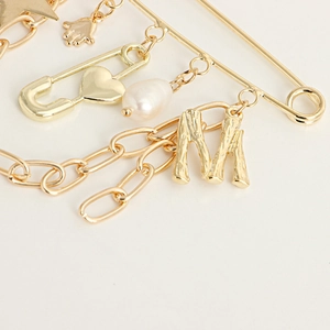 Detail of gold pin brooch featuring star, letter M, pearl, and chain charms