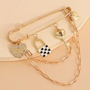 Detail of vintage gold safety pin brooch with checkerboard lock, key, and heart charms