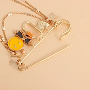 Détail d'une broche épingle à nourrice dorée avec smiley jaune, étoiles et chaînes à glands