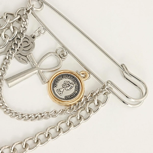 Close-up of punk style silver brooch with rose, cross, and coin pendants on metal chains