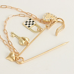 Detail of gold safety pin brooch with checkerboard lock, key and sparkling heart charms