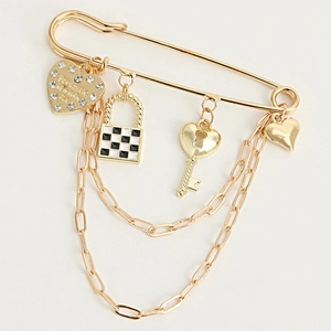 Detail of a gold safety pin brooch with checkered heart charms and metallic chains