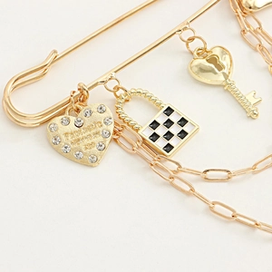Macro shot of gold pin brooch featuring checkered lock, crystal heart, and key charms