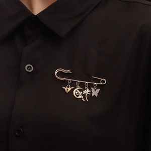 Elegante spilla a balia dorata con ciondoli indossata su camicia nera, dettaglio di lusso