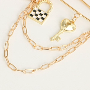 Detail of gold chain brooch with checkerboard lock and heart key charms on white background