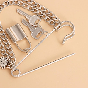 Detail of silver punk chain pin with padlock, keys and sun pendant on pink background