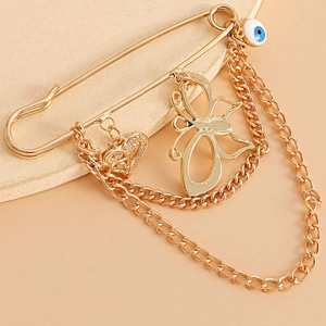 Détail d'une broche papillon dorée avec pendentifs cœur, œil bleu et doubles chaînes