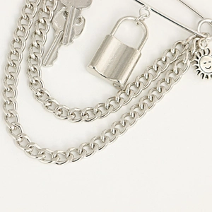 Close-up of punk silver brooch with layered chains, padlock, key and sun face charms