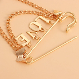 Detail of gold LOVE brooch featuring chain link with heart and butterfly charms
