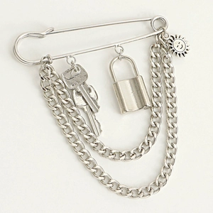 Detail of silver punk safety pin brooch featuring hanging Cuban chains, keys and padlock