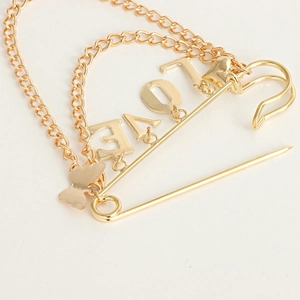 Detail of gold LOVE brooch with hanging chain, butterfly charm and safety pin design