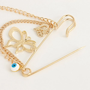 Vue détaillée d'une broche épingle dorée avec pendentifs papillon, cœur et œil porte-bonheur