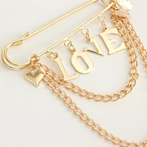 Close-up of golden LOVE brooch with heart and butterfly charms on white background