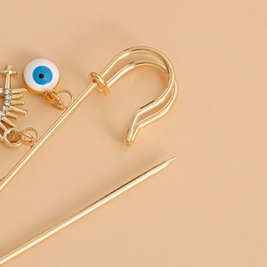 Macro detail of golden evil eye safety pin brooch with enamel charms and rhinestones