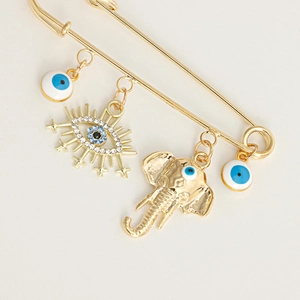 Detailed view of golden safety pin brooch featuring evil eye charms and an elephant pendant