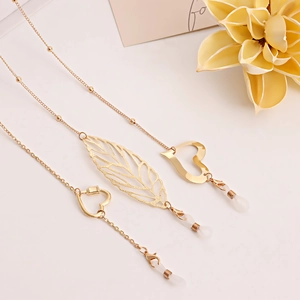 Trois chaînes de lunettes dorées avec pendentifs feuilles et cœurs sur fond blanc