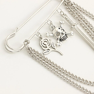 Close-up of punk style silver brooch with chain tassels, skull, rose, and sword charms