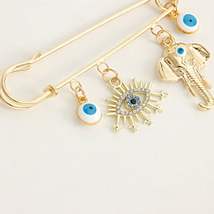 Macro view of gold pin brooch featuring Nazar evil eye and elephant pendants with rhinestones