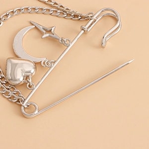 Close-up of silver safety pin brooch with heart, moon, and star charms on a metal chain
