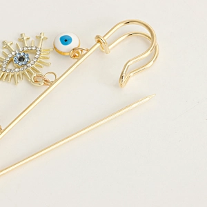 Macro detail of gold safety pin brooch with nazar evil eye beads and crystal pendant