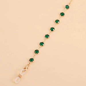 Macro detail of gold eyewear chain with green crystals and clear silicone loops