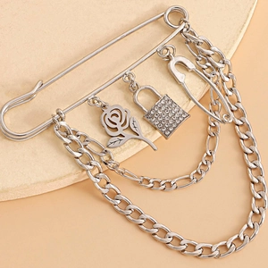 Detail showing a silver rose pendant, padlock with crystals and layered chains on a safety pin