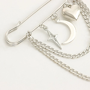 Macro shot of silver safety pin brooch with heart, moon, and star charms on metal chains