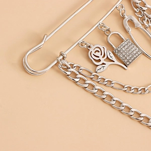 Detail of silver punk rose pendant with rhinestone padlock and metal chains on a safety pin