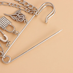 Detail of silver rose pendant and rhinestone padlock charms on a punk safety pin brooch