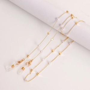Detail view of gold glasses chain with white pearls and square beads on a white holder