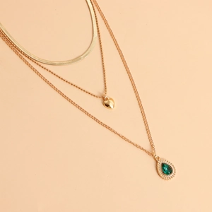 Detail van drielaagse gouden ketting met groene druppelsteen en hartvormige hanger
