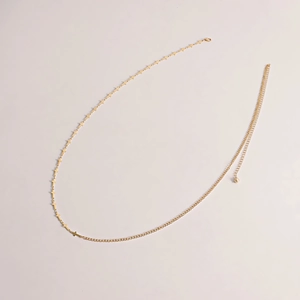 Détail de la chaîne de taille dorée avec croix et élégant pendentif perle sur fond blanc