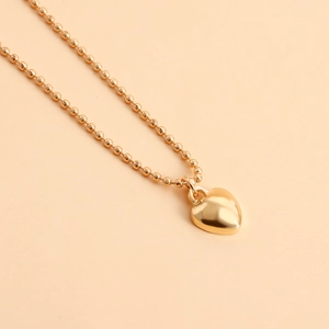 Detail van de gouden kogelketting met gepolijste hartvormige hanger en metaalglans